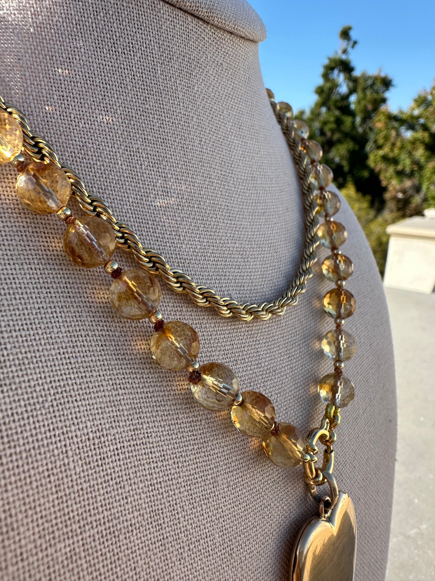 Necklace with gold chain and clear beads on a mannequin against a blue sky.