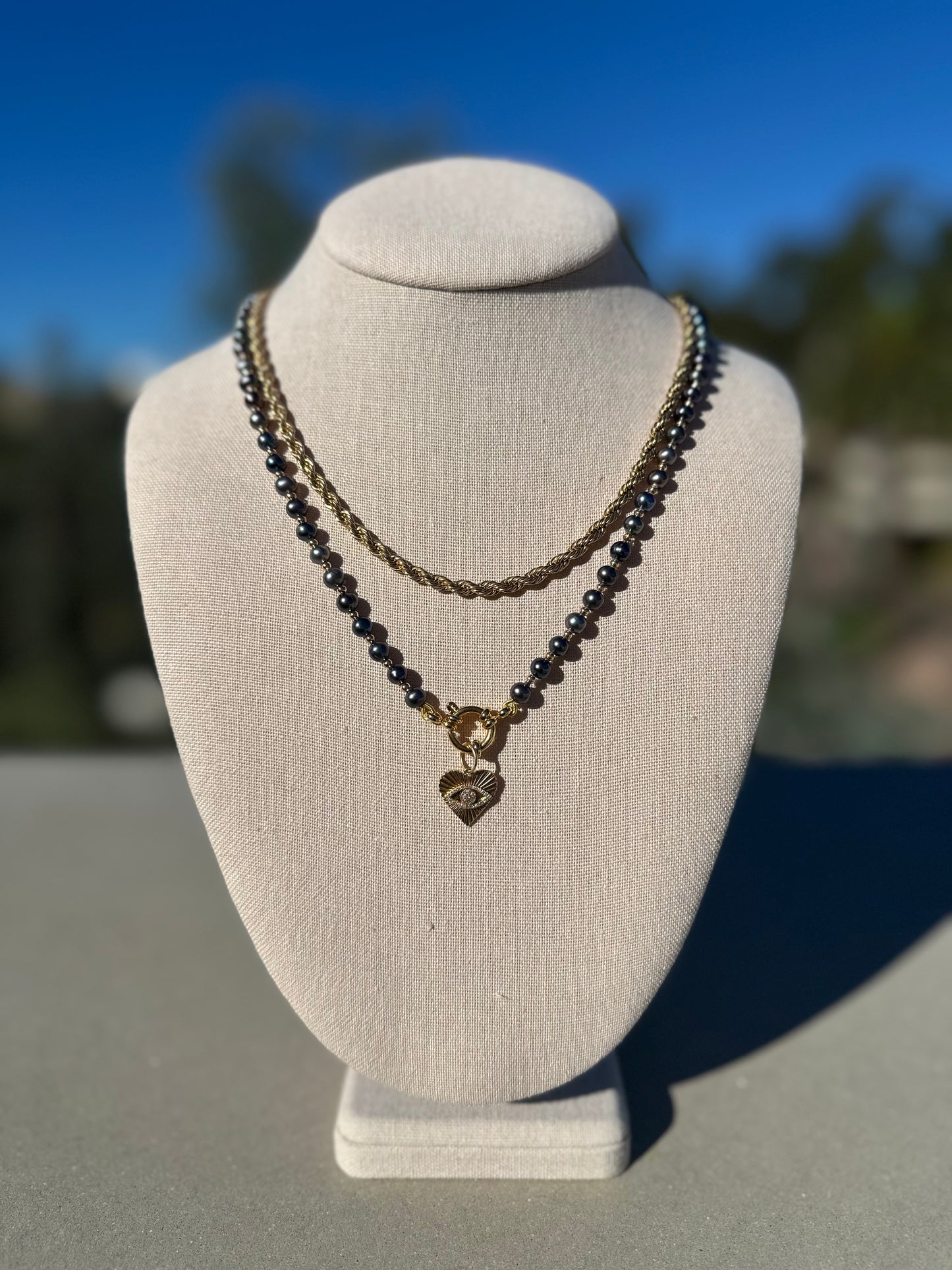 Black freshwater pearl necklace shown with separate gold chain and charm, charm not included.