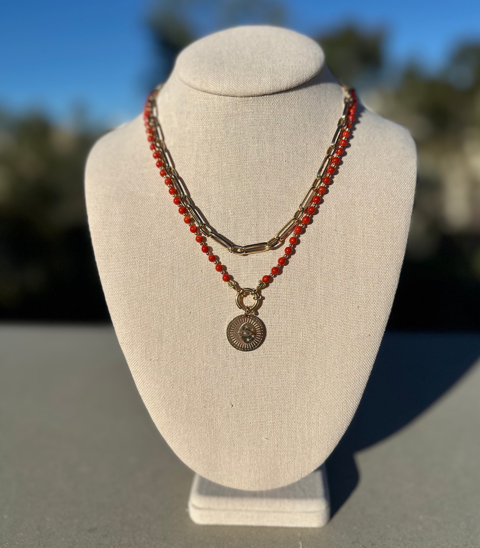Coral beaded necklace shown with separate gold chain and charm for styling, charm and chain not included.