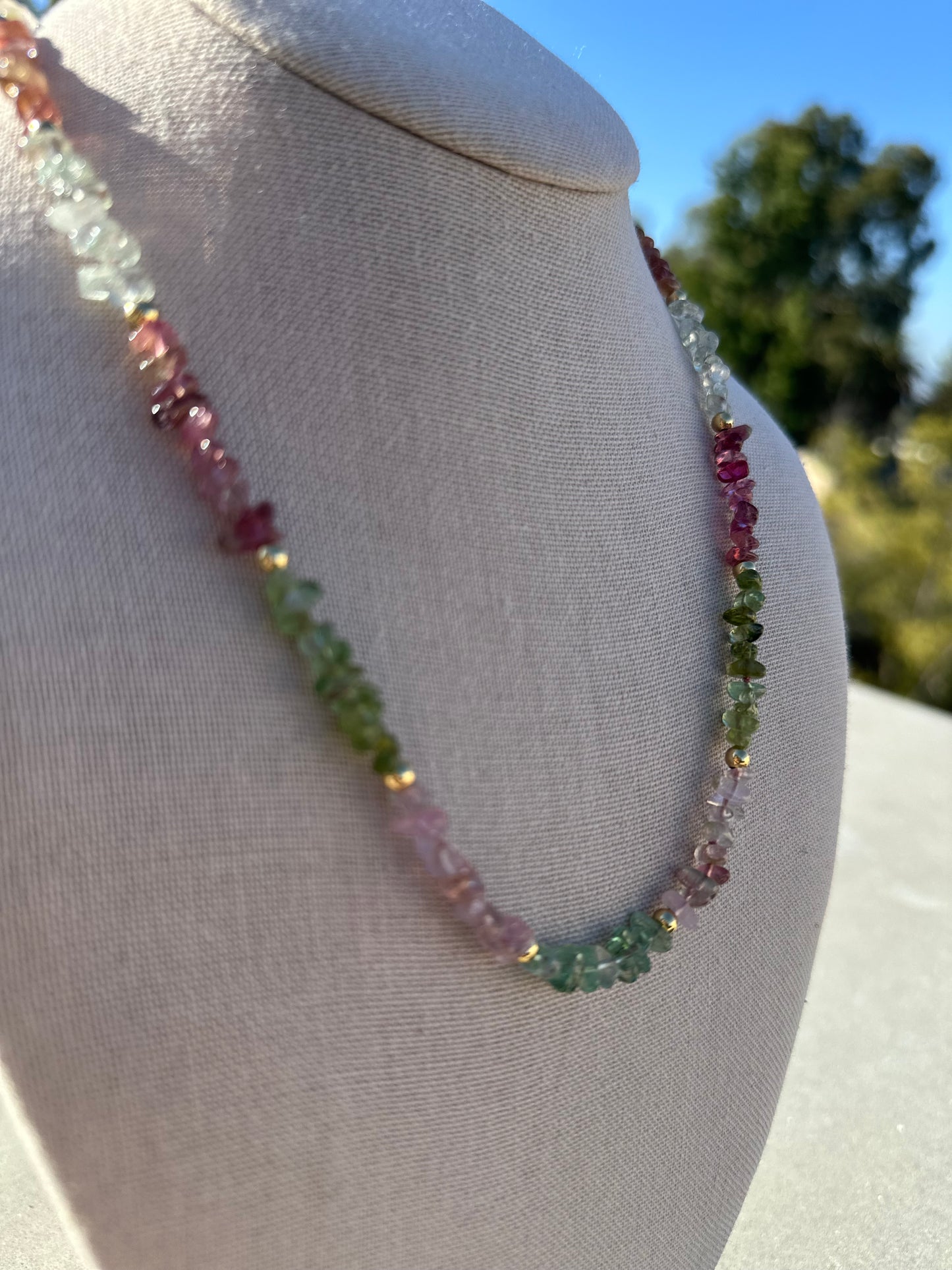 Close-up of multi-color tourmaline beads showing 2–6 mm size variation and gold-plated accents.
