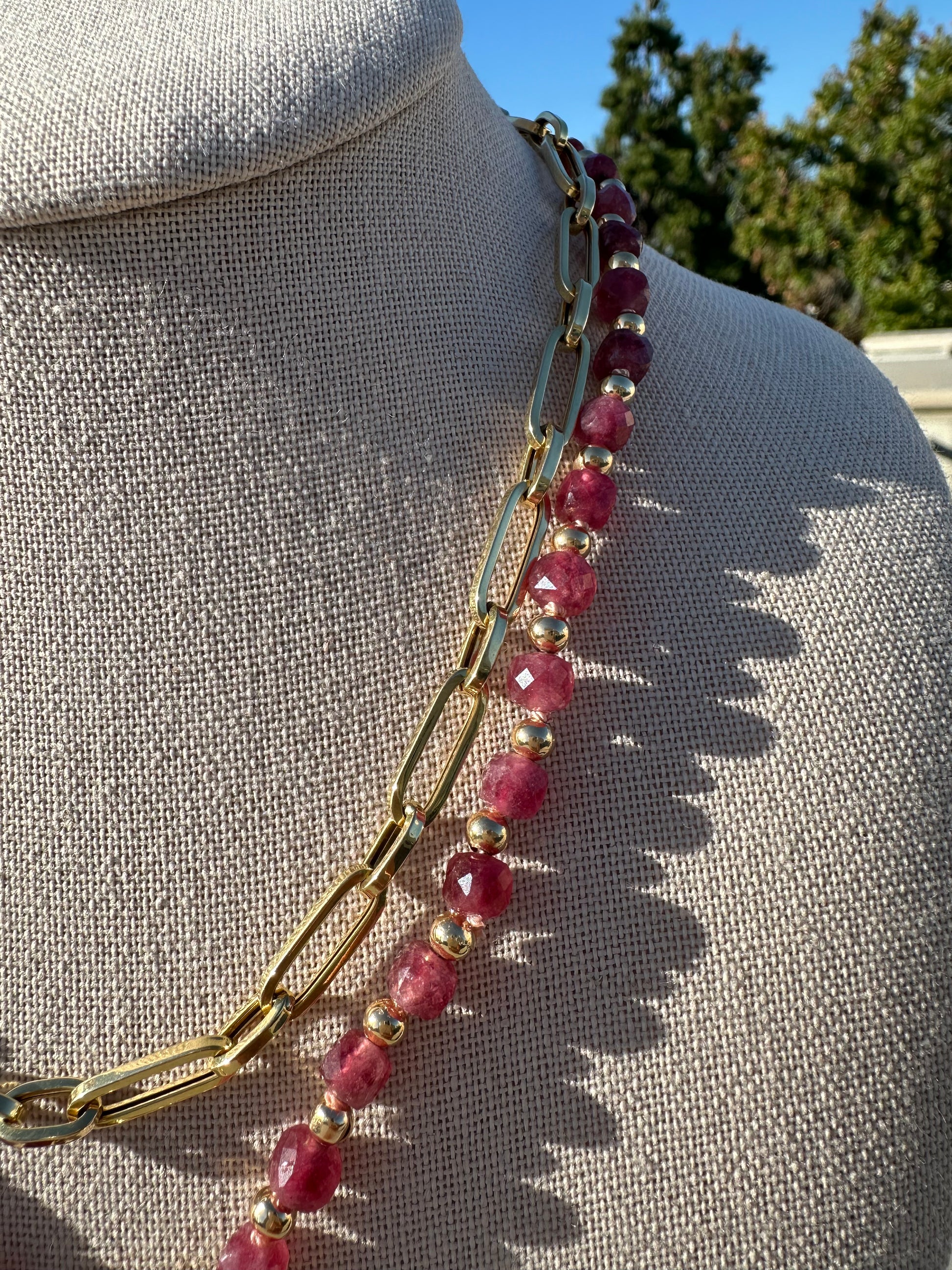 Ruby beaded necklace and gold chain under natural light showing color variation of faceted stones.

