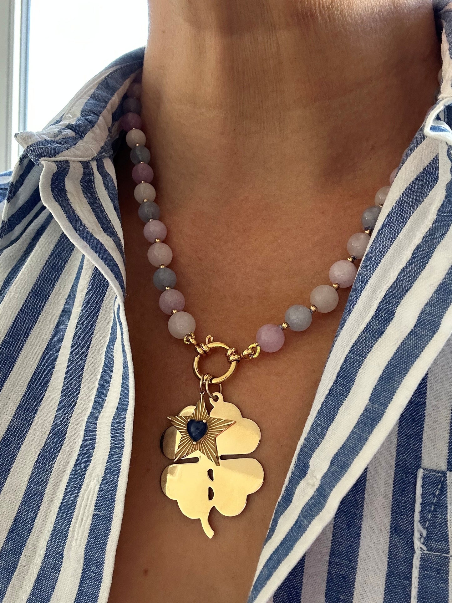 Morganite necklace styled with layered gold chain and black clover charm on model