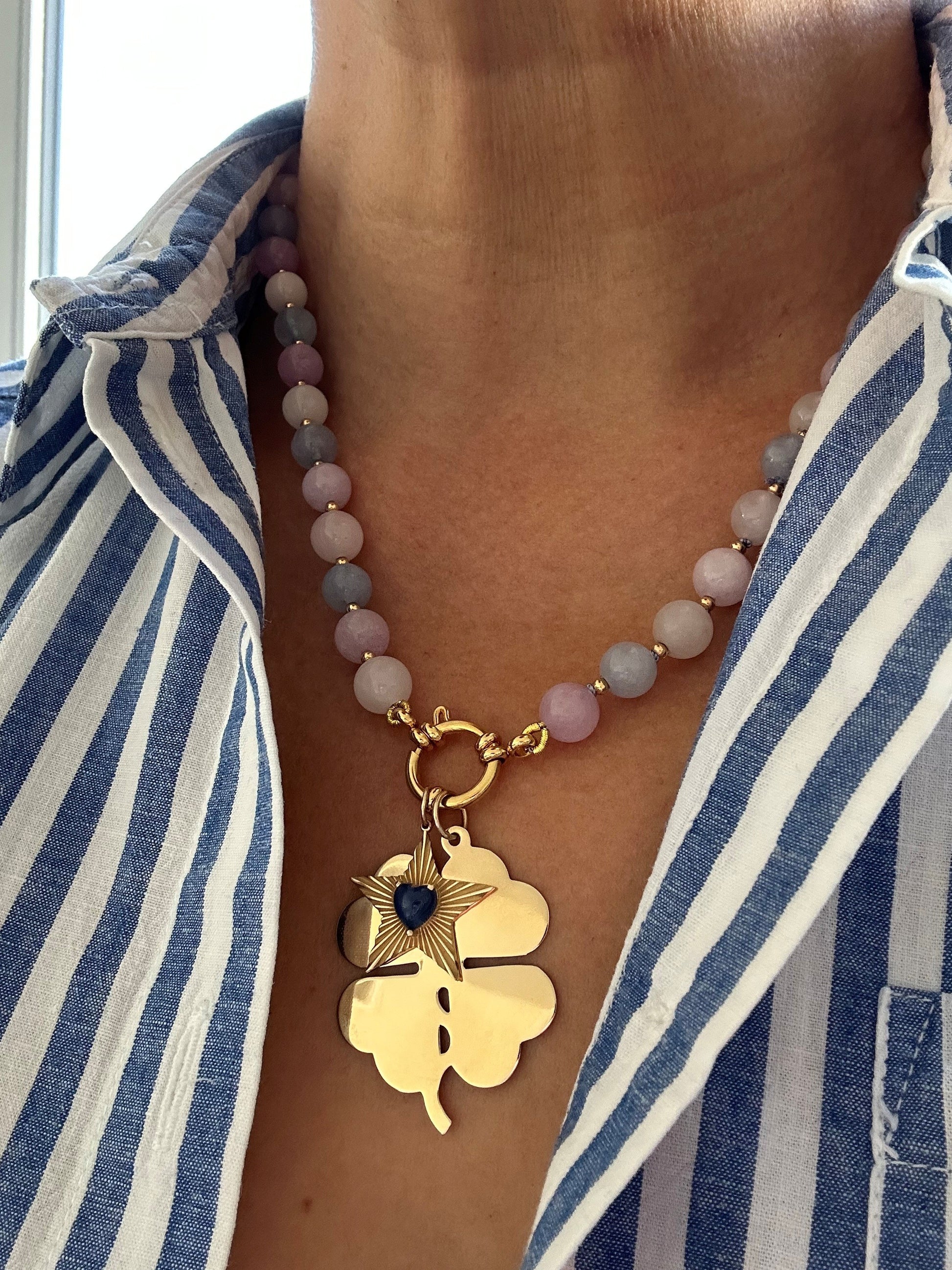 Morganite necklace styled with layered gold chain and black clover charm on model