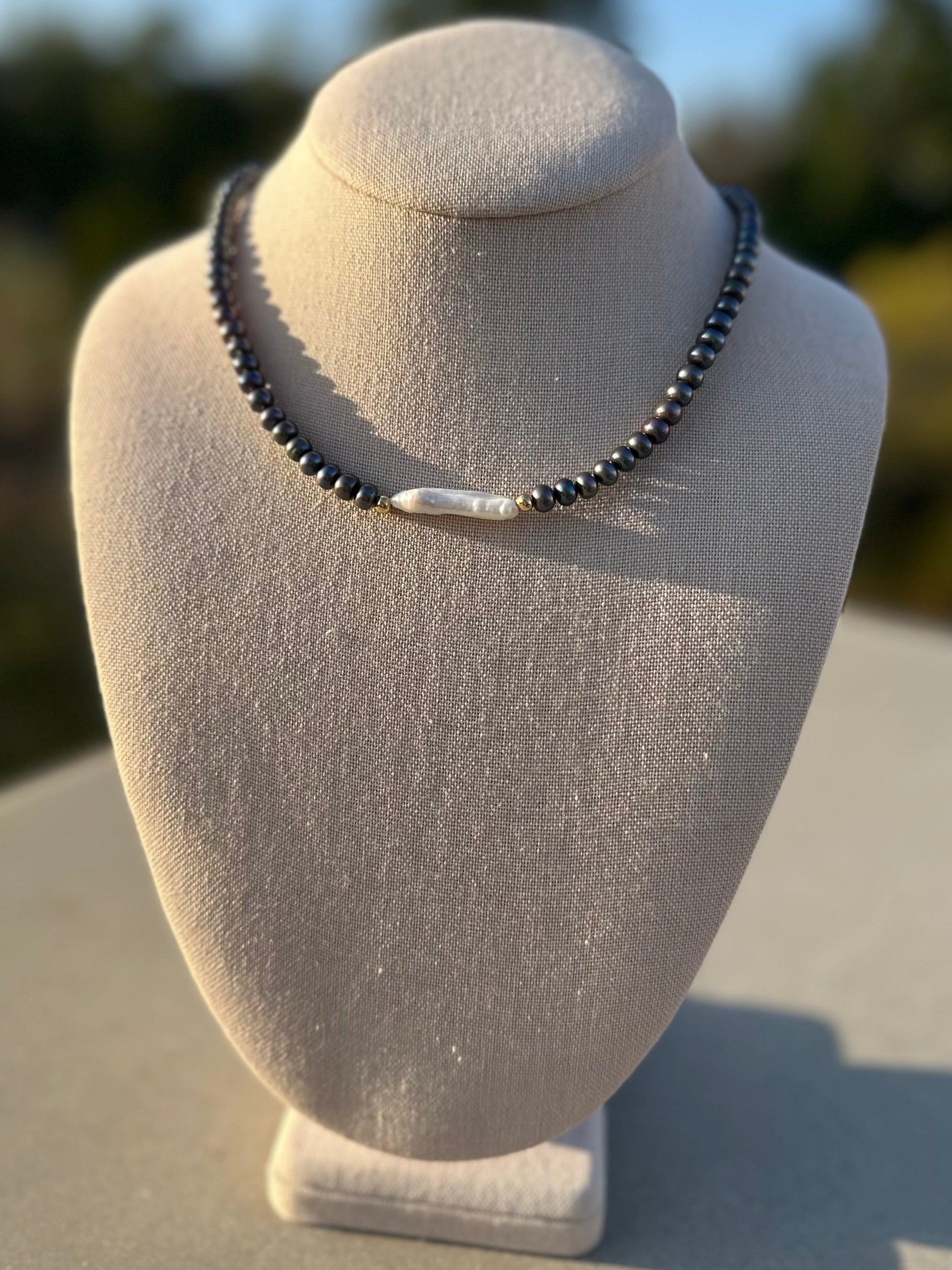Hand-strung black pearl necklace with gold clasp displayed under sunlight