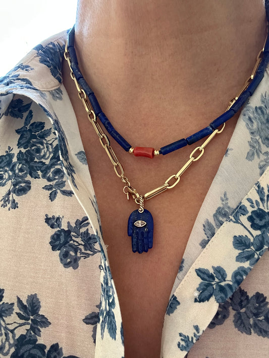 Lapis and coral necklace layered with gold chain and blue charm pendant on model in floral shirt