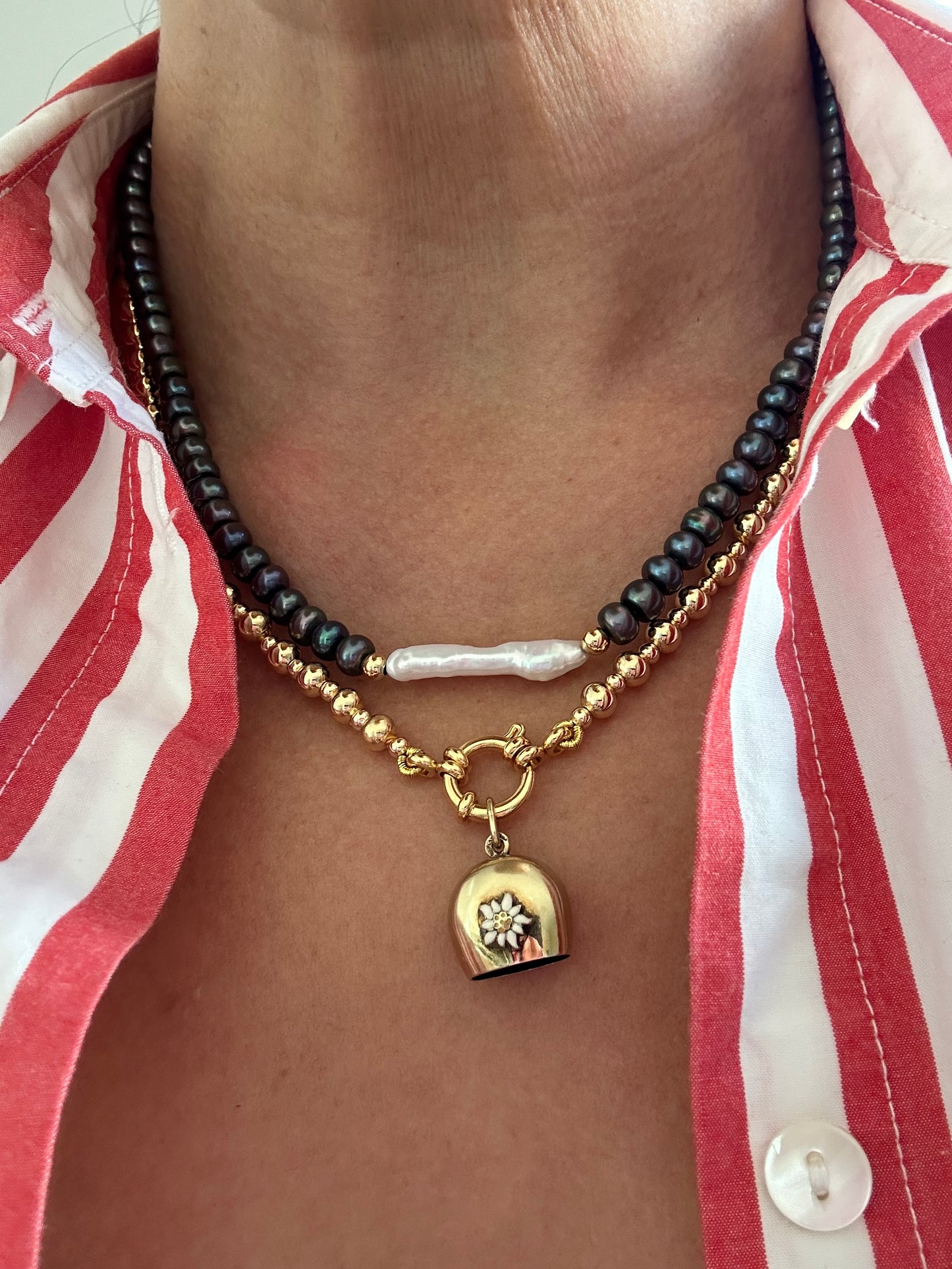 Black and white pearl necklace styled with layered gold chain and charm on model wearing striped shirt