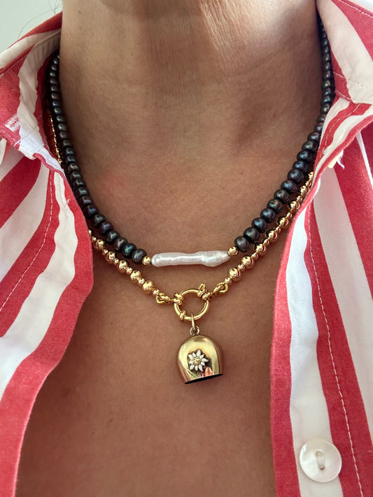 Black and white pearl necklace styled with layered gold chain and charm on model wearing striped shirt